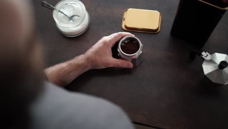 unrecognizable person seen from behind puts coffee with a spoon on an italian coffee maker and closing it, with a jar of sugar on the frame