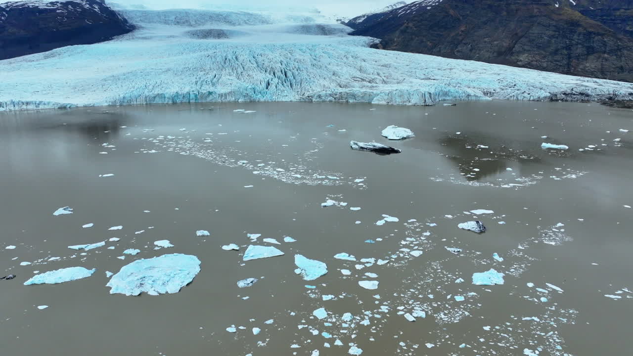 Massive icebergs drifting across glacial lake near Vatnajokull glacier, revealing pristine arctic landscape under dramatic sky with mountain backdrop
