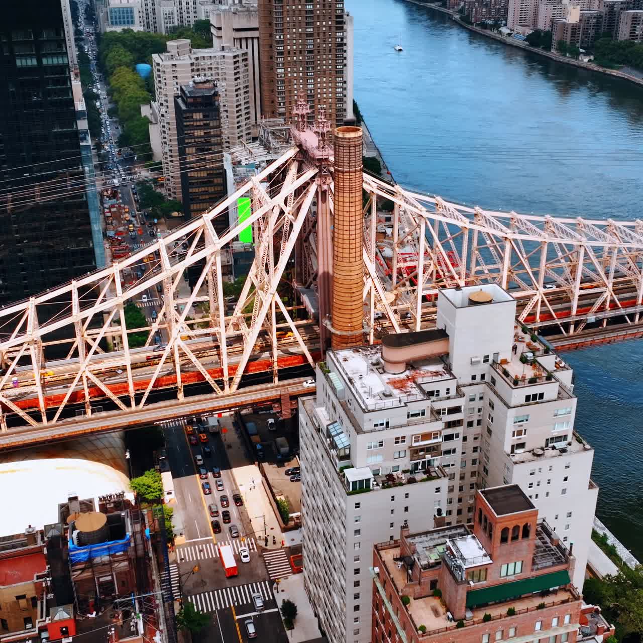 One of the waterfront sides of Queensboro Bridge with huge buildings surrounding it. Lively highway is under the bridge. Top view