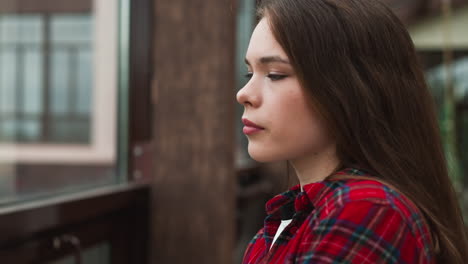 a young woman with long brown hair and a red plaid shirt looks away from the camera with a serious expression.