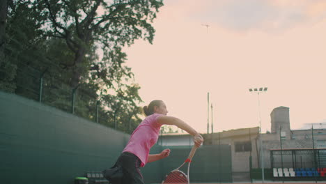 slow-motion side view of a young athlete trains the serve of the tennis ball. a teenage athlete is playing tennis on a court. an active girl is powerfully hitting a ball during sport practicing