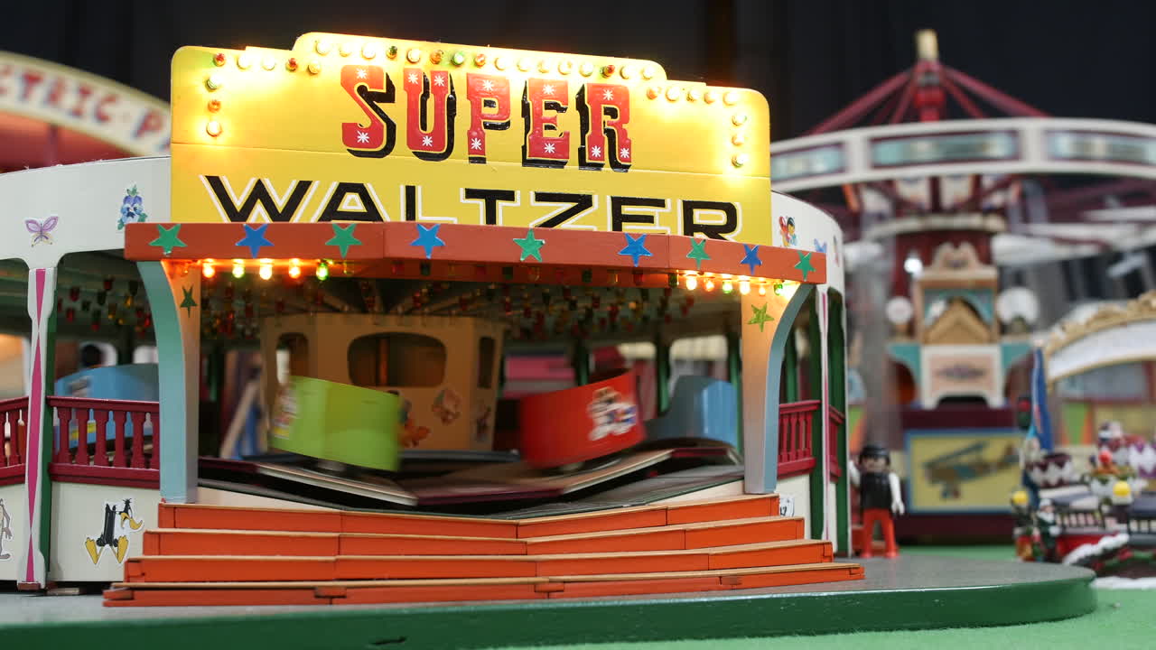 A model waltzer ride with rotating cars and a glowing “Super Waltzer” sign is capturing detailed amusement park features with bright trim and painted decor