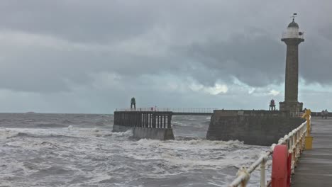 wide angle shot of waves crashing along the walls at whitby harbour lighthouse