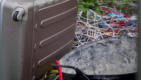 electrical cable, a suitcase and a builder's trug illegally fly tipped on the side of an english road and other rubbish