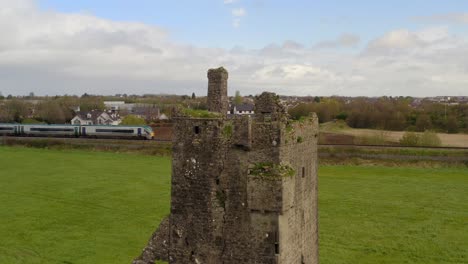 Srah-castle-stands-in-solitude-as-train-passes-on-rail-tracks-behind,-aerial