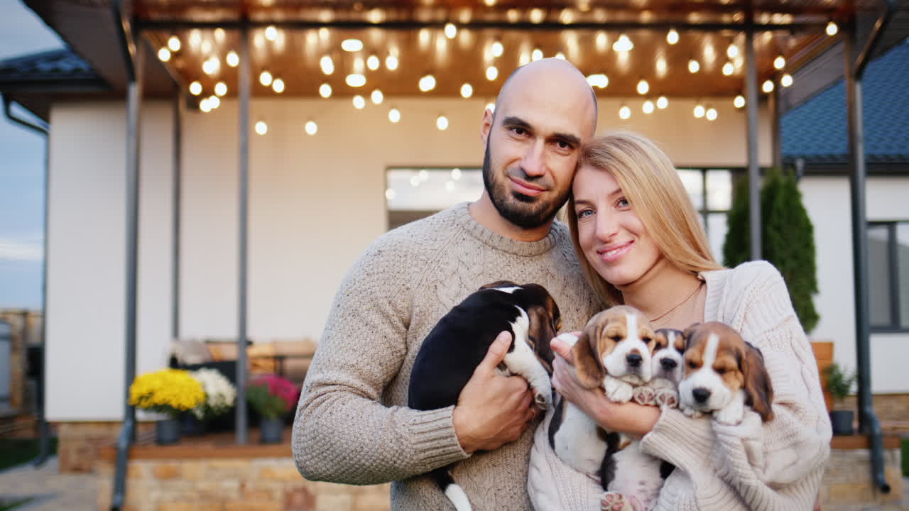 집 앞 에 있는 젊은 가족 이 손 에 여러 마리 의 강아지 를 들고 있다