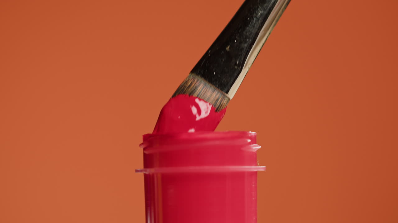 Pincel sumergiéndose en bote de pintura rosa vibrante