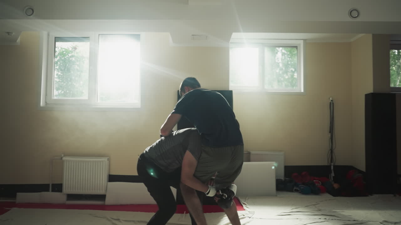 파트너를 던지고 스포츠 클럽 바닥에 주먹을 니다. 강한 운동선수들은 빛 체육관에서 스파링하는 동안 싸니다. 무술 기법