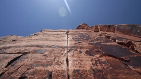 man climbing on steep red rock in utah usa, low angle view of climber, ropes and cliff on hot sunny day