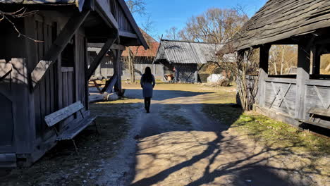 woman walking through old wooden structures with farmhouse in traditional farming village