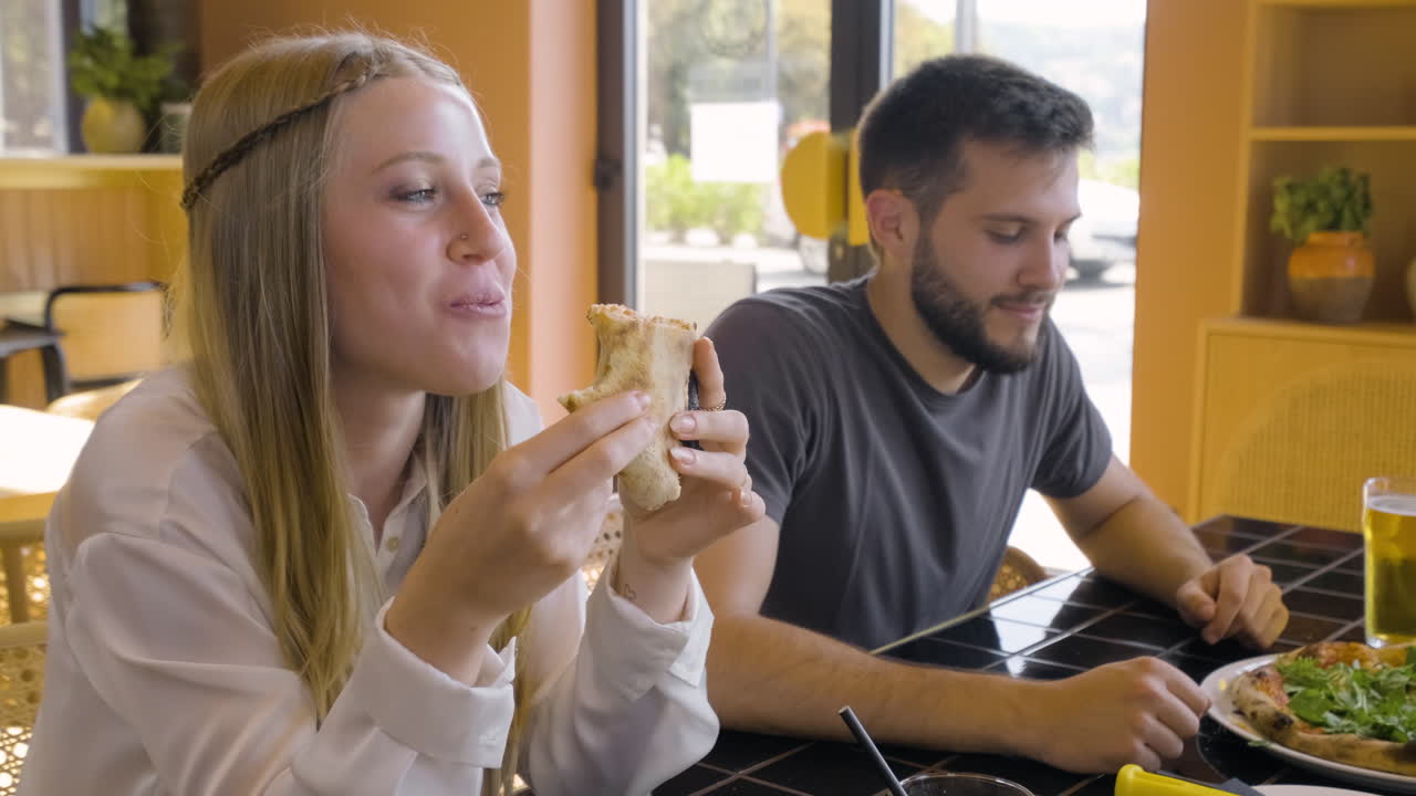 chica rubia comiendo pizza sentada en una mesa de restaurante con sus amigos