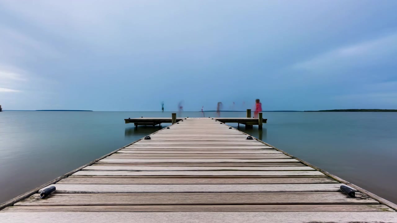 Vista centrata dal basso di un molo di legno invecchiato che si estende in un lago liscio e riflettente sotto nuvole suggestive e la calda luce del tramonto.