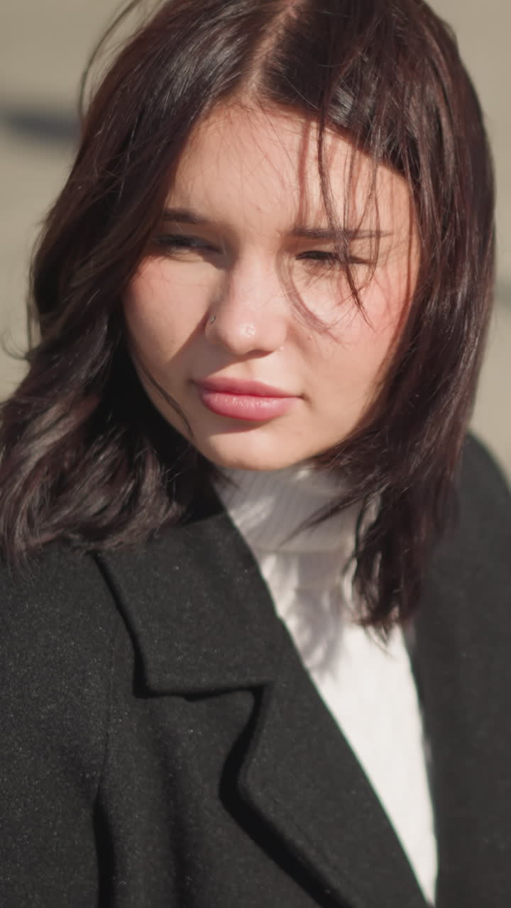 앞을 바라보기 위해 회전하는 자신감있는 여성의 클로즈업, 빛이 그녀의 얼굴과 미묘한 코 반지를 강조하고, 그녀가 왼쪽으로 회전할 때 땅에 던진 그림자, 흐릿한 도시 배경