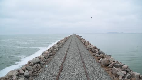 low forward aerial along straight train track by water in argentina