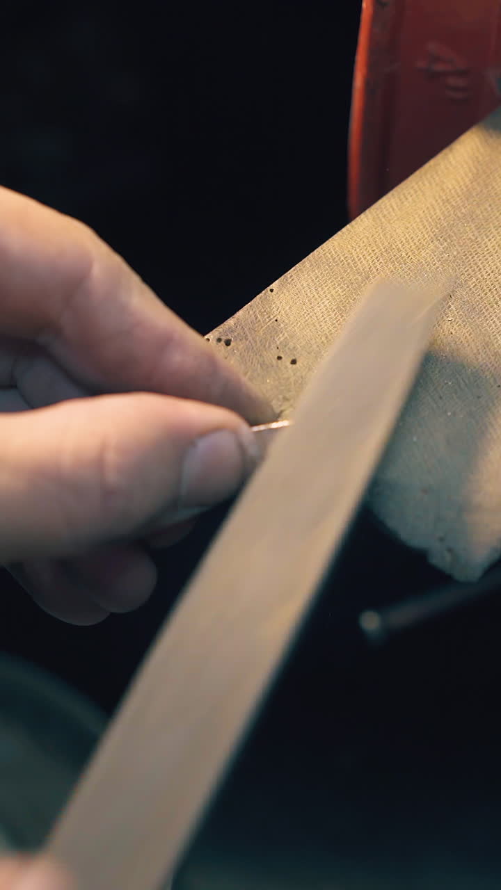 CU shot: skilled jeweler files white gold bar workpiece with rasp at workplace in manufacturing workshop close view