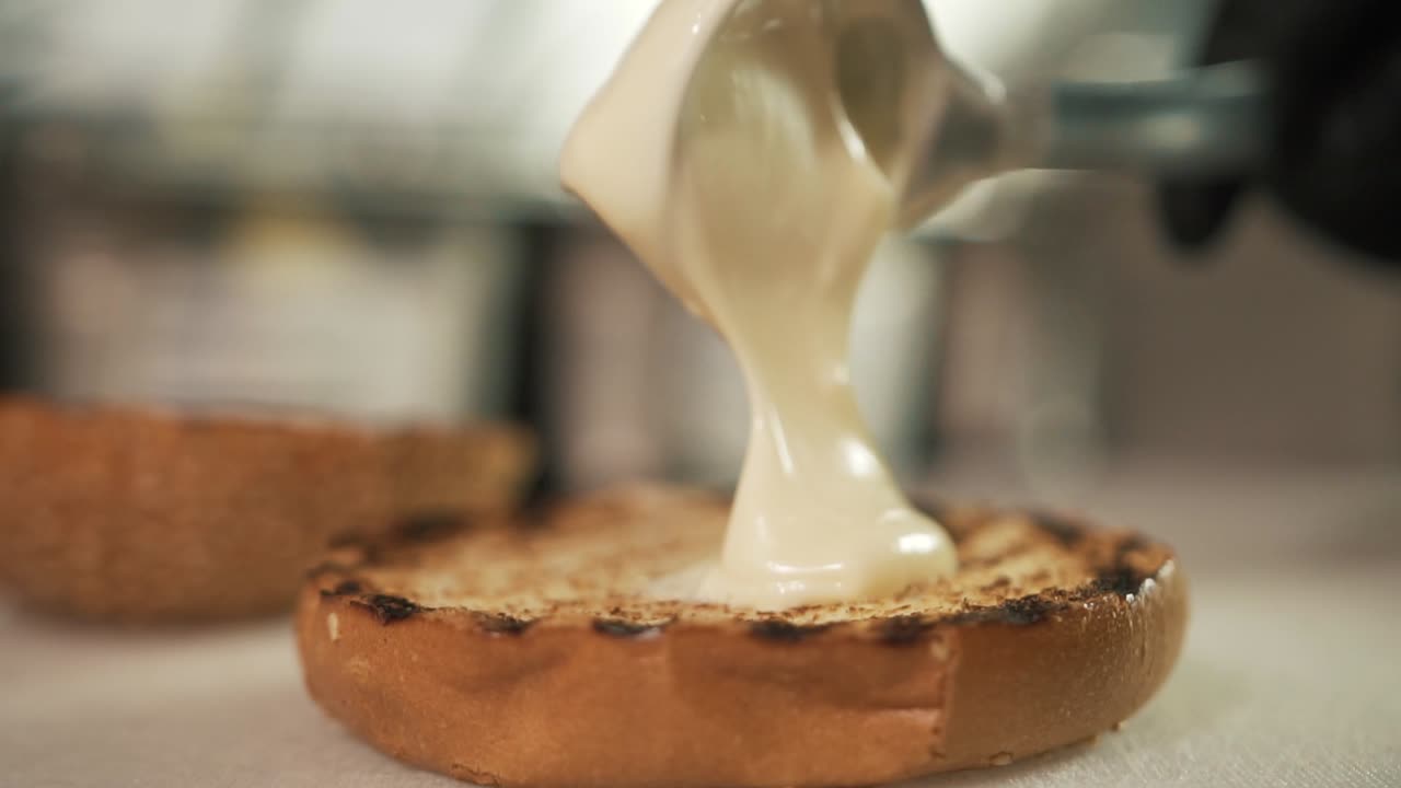 Chef adds mayonnaise sauce to burger bread with spoon and black glove. Slow-motion close up