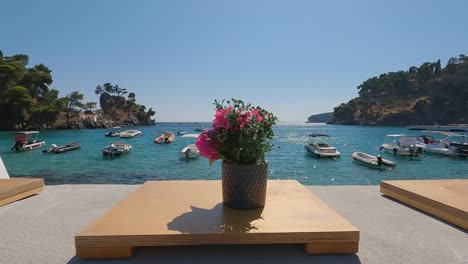 dolly shot along flowerpots on beachfront promenade, boats moored on turquoise water bay, parga