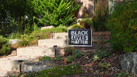 black lives matter yard sign on front porch of house surounded by weeds