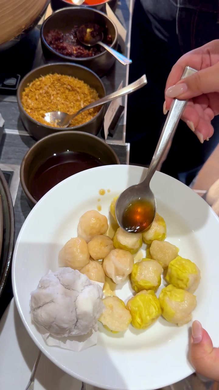 Una persona versa salsa scura su un piatto di shumai al vapore e panini al vapore con maiale.