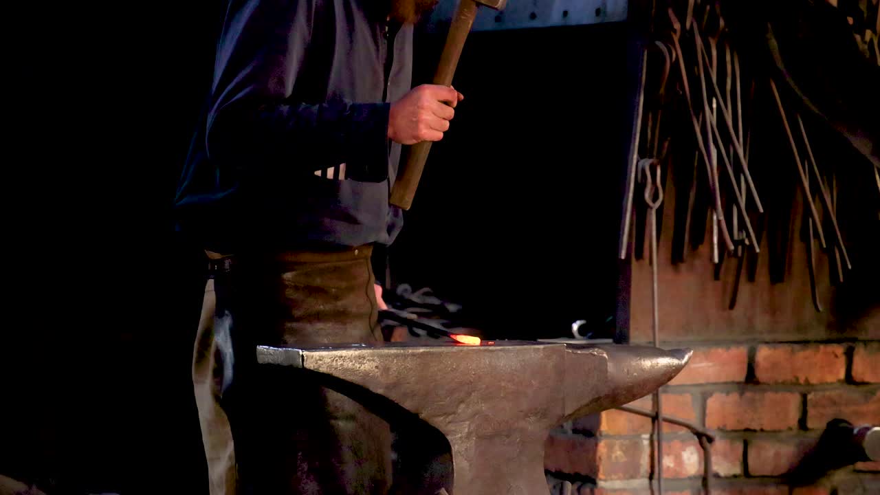 un herrero martilla metal en un yunque en una forja débilmente iluminada, rodeada de herramientas y paredes de ladrillo