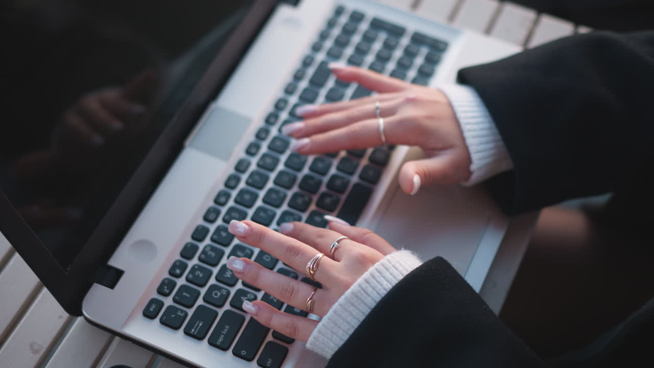 화면에 반사되는 끔한 손과 우아한 반지로 노트북 키보드에서 타이핑하는 손의 클로즈업, 기술에 능숙하고 전문적인 분위기를 보여줍니다.