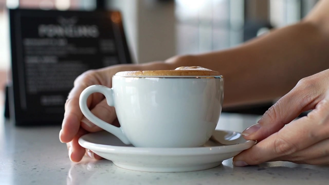 Mani che posizionano una tazza e un piattino bianchi sul bancone del caffè, centrando il caffè con schiuma.