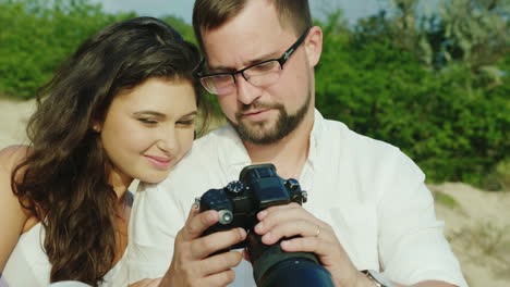 a young couple looks at the pictures on a digital camera sit next to the beach great memories from h