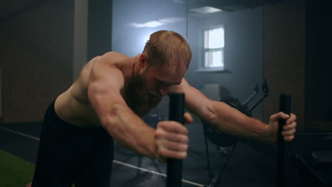 a powerful man pushes a heavy weight trolley in the gym in slow motion. bearded man with vapor on his body trains