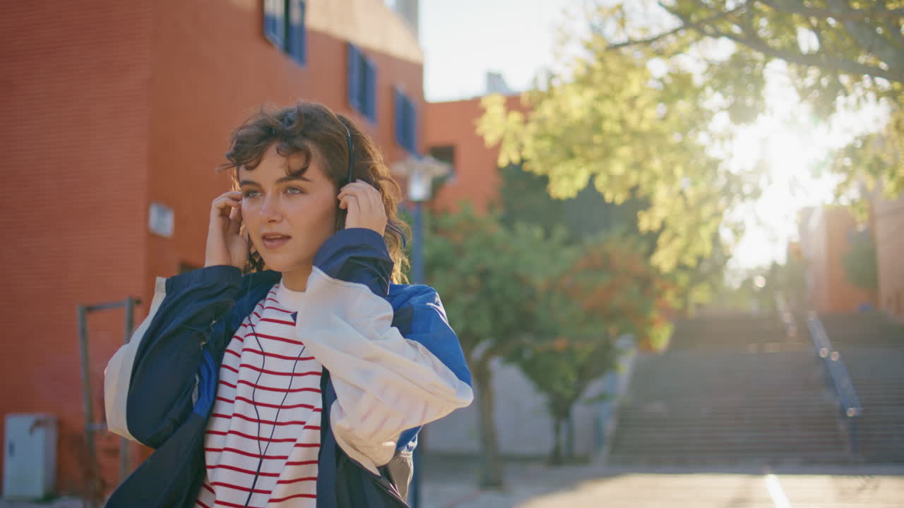 joven melómano disfrutando de la música en los auriculares en la calle soleada caminando de cerca.