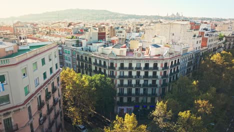 drone shot over the rooftops of colorful buildings in barcelona, showing tree-lined streets and distant hills on the horizon