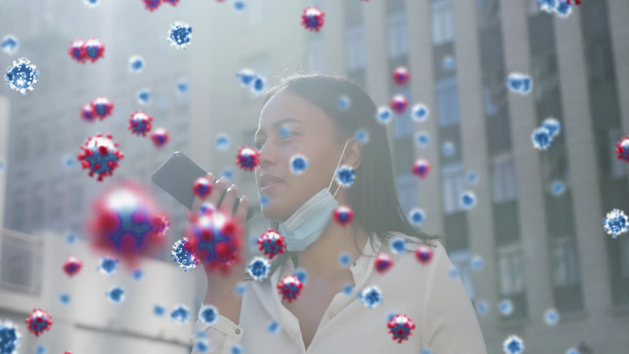 Multiple covid-19 cells floating against woman with lowered face mask talking on smartphone