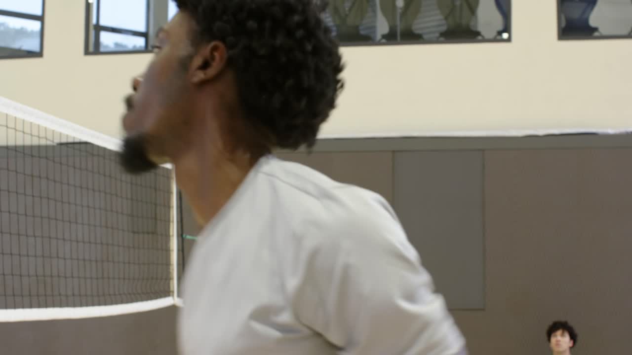 Diverse men practicing in gym with server tossing red white blue volleyball as tall player bumping