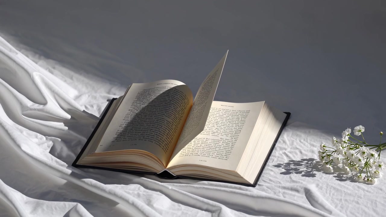 Libro aperto con pagine che si girano e fiori bianchi nella luce soffusa