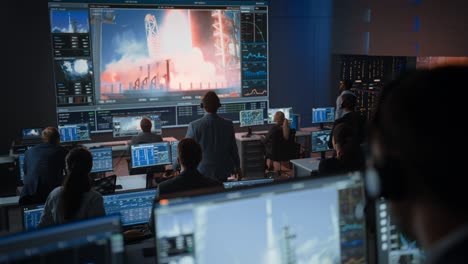 group of people in mission control center witness successful space rocket launch. flight control employees sit in front computer displays and monitor the crewed mission. team stand up and clap hands.