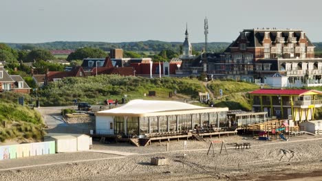 Beautiful-aerial-shot-of-a-very-old-bathing-pavilion-and-modern-beach-clubs-along-the-Dutch-coast-during-sunset