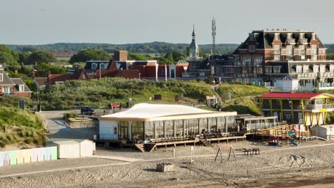 Wunderschöne-Luftaufnahme-Eines-Sehr-Alten-Badepavillons-Und-Moderner-Strandclubs-Entlang-Der-Niederländischen-Küste-Bei-Sonnenuntergang