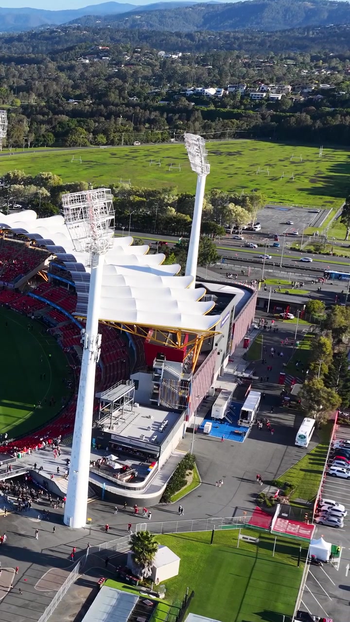 High-angle drone shot captures a professional sports arena and surrounding landscape in bright daylight.