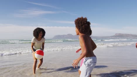 madre afroamericana y sus hijos jugando con una pelota en la playa
