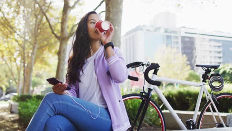 asian woman wearing earphones listening to music and drinking takeaway coffee