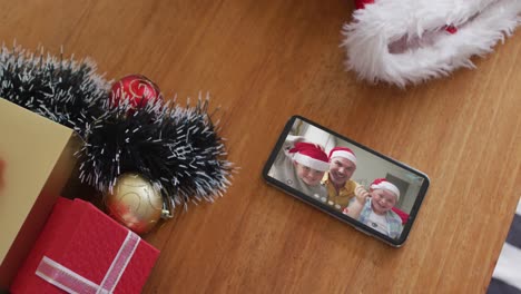 Familia-Caucásica-Sonriente-Con-Sombreros-De-Papá-Noel-En-Videollamada-Navideña-En-Un-Teléfono-Inteligente