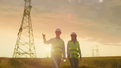 Ingeniería-Trabajando-En-Una-Torre-De-Alto-Voltaje-Verifique-La-Información-En-La-Tableta-Dos-Empleados,-Hombre-Y-Mujer