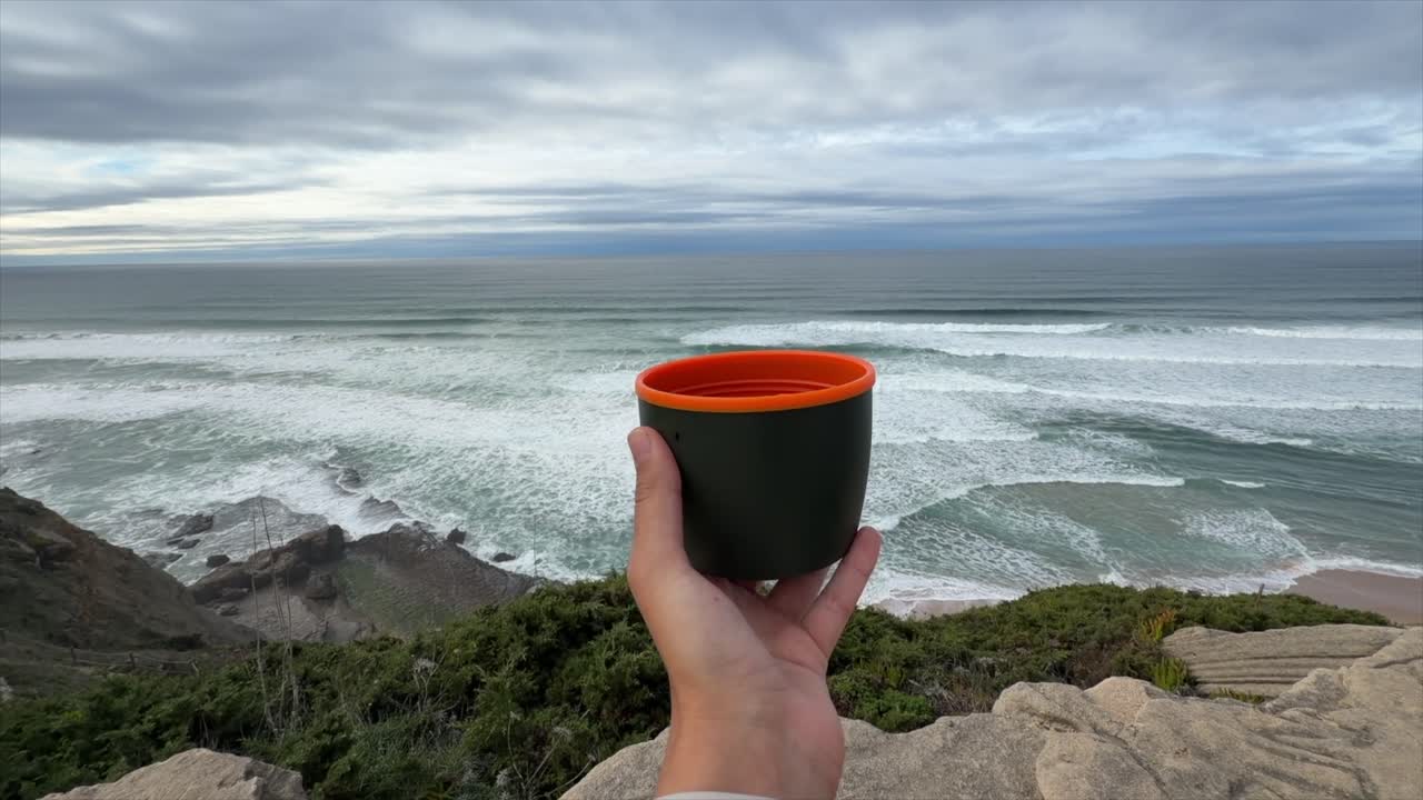 Mano che tiene una tazza di caffè con vista sulle onde dell'oceano e sulla scogliera