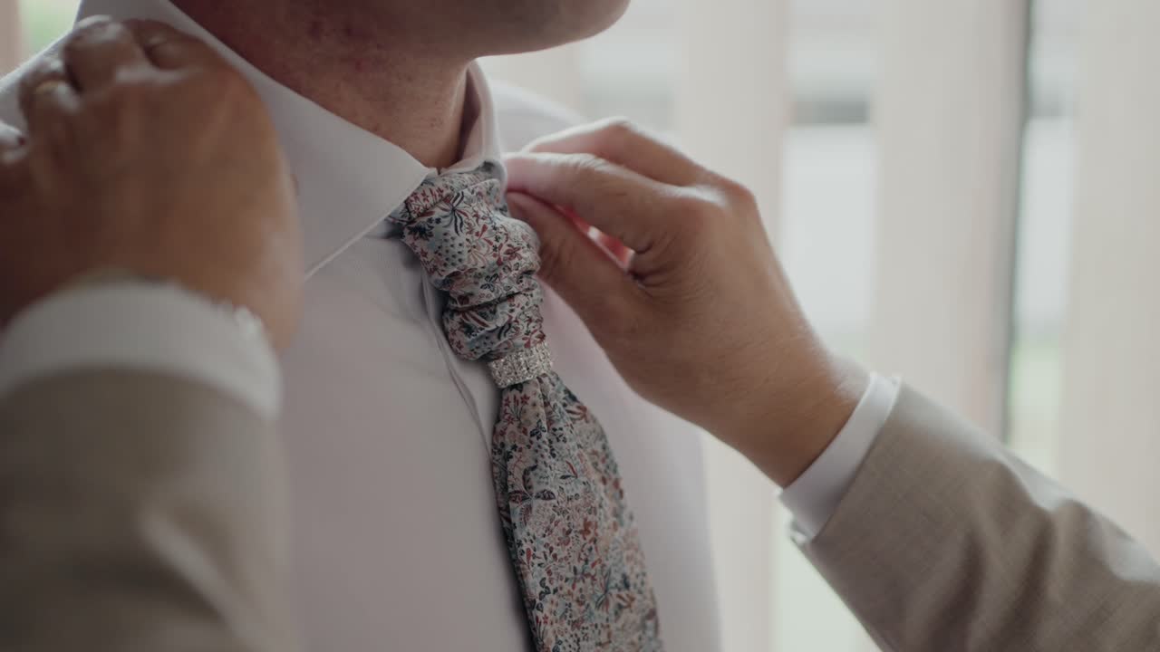 primer plano del novio ajustando su corbata floral, capturando un momento de preparación y elegancia