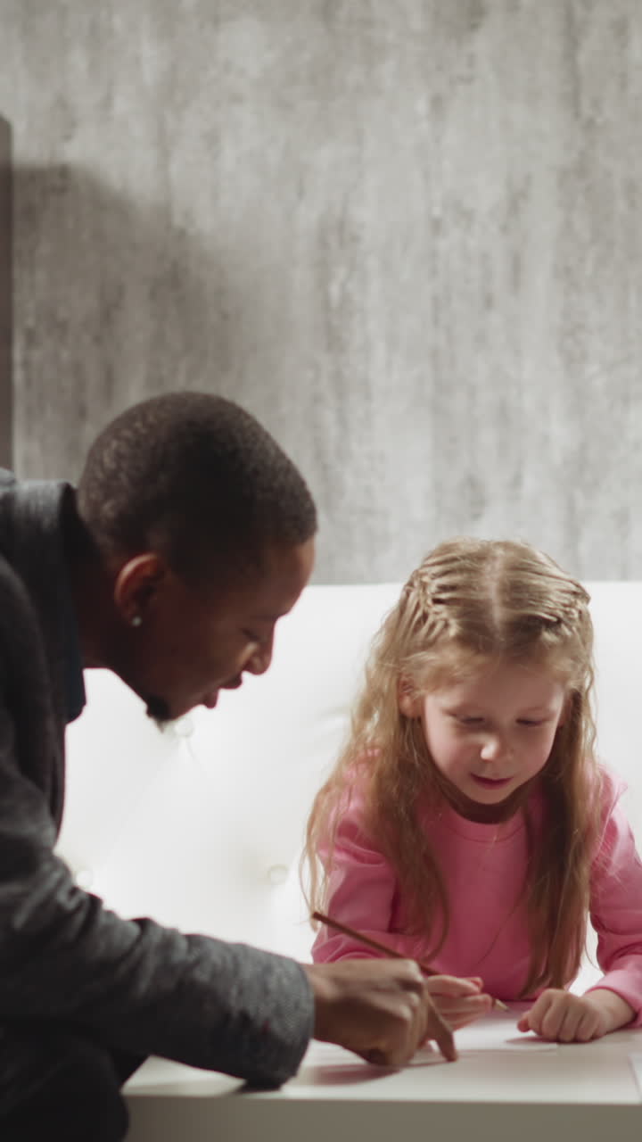 Careful African-American teacher writes letters by finger on table and children try to understand studying at home lesson with skilled tutor slow motion