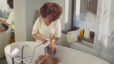 african american mother washing hair of little son in bathroom