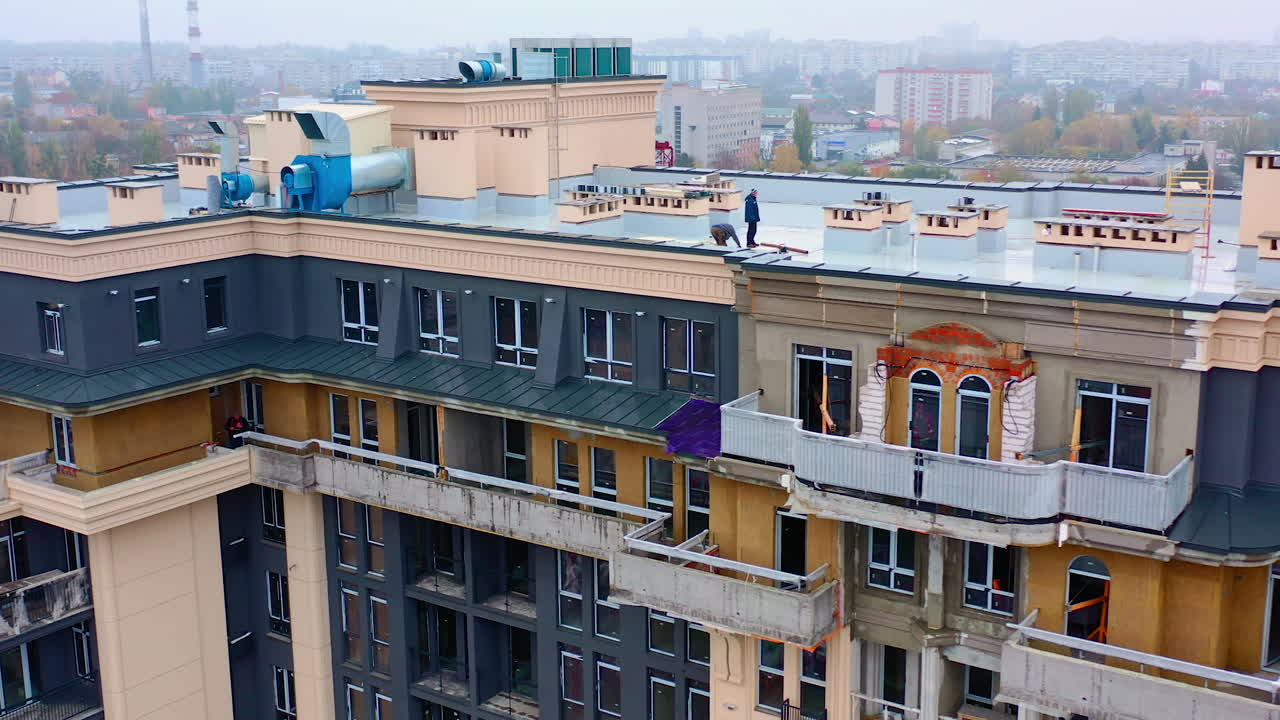 Building of a new tower house. Workers on the roof of multistorey building during the construction on the cityscape. Aerial view.