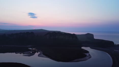 Aerial-drone-birds-eye-view-of-coastal-beach-landscape-at-twilight-sunrise,-Devon-England