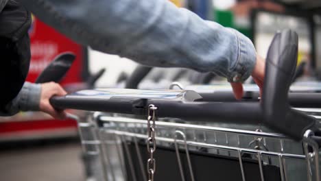 Foto-De-Una-Mujer-Con-Una-Chaqueta-De-Jeans-Azul-Que-Usa-Una-Moneda-De-1€-Para-Alquilar-Un-Carrito-De-Compras-En-Una-Tienda-De-Comestibles-En-Alemania-Para-Comprar-Alimentos,-Bebidas,-Frutas-Y-Otras-Cosas