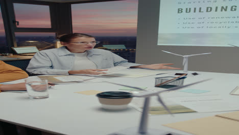 male and female engineers sitting behind the table during office meeting in the evening, having discussion about wind energy project with team. vertical format video