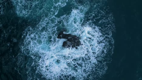 Aerial-drone-footage-of-the-sea,-showing-waves-flowing-around-a-rock